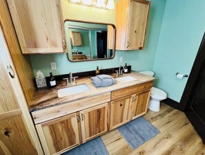 A bathroom with a wooden vanity, two sinks, a mirror, and a toilet. - The Loess Hills Cottage (Onawa)