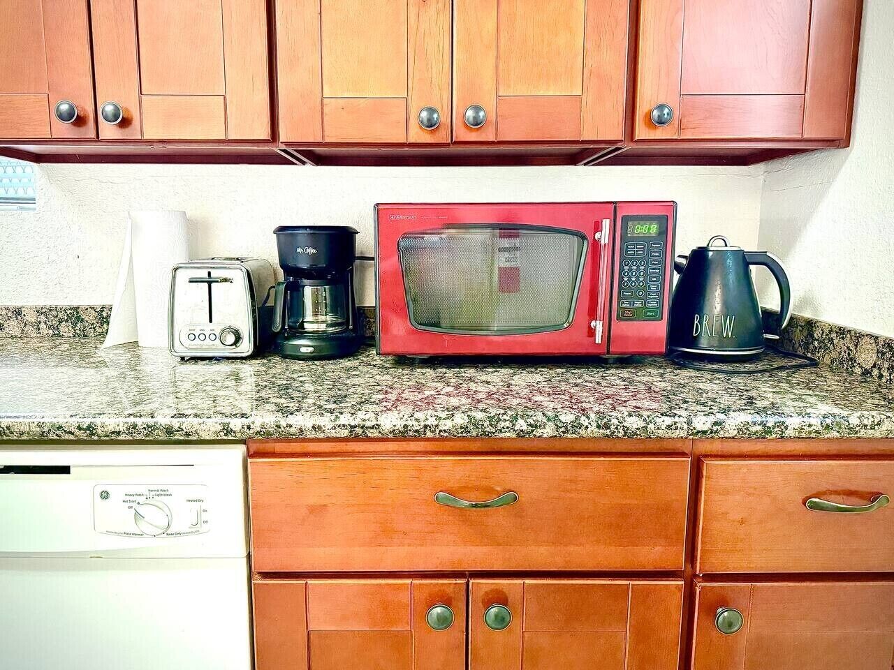 A kitchen with wooden cabinets, a toaster, a red microwave, a coffee maker, and a dishwasher.