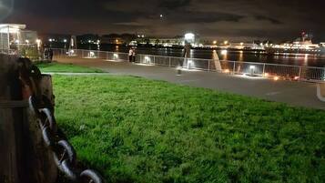 A nighttime view of a riverside walkway with a grassy area and a metal fence.
