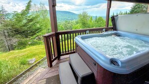 Ein Whirlpool auf einer Holzterrasse mit Blick auf Wald und Berge.