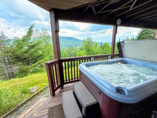 Ein Whirlpool auf einer Holzterrasse mit Blick auf Wald und Berge.