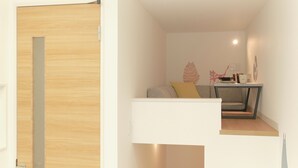A modern, compact room with a wooden door, a small seating area with cushions, and a small table with a lamp. - Gaia BOSCO by Tranova (Tokyo)