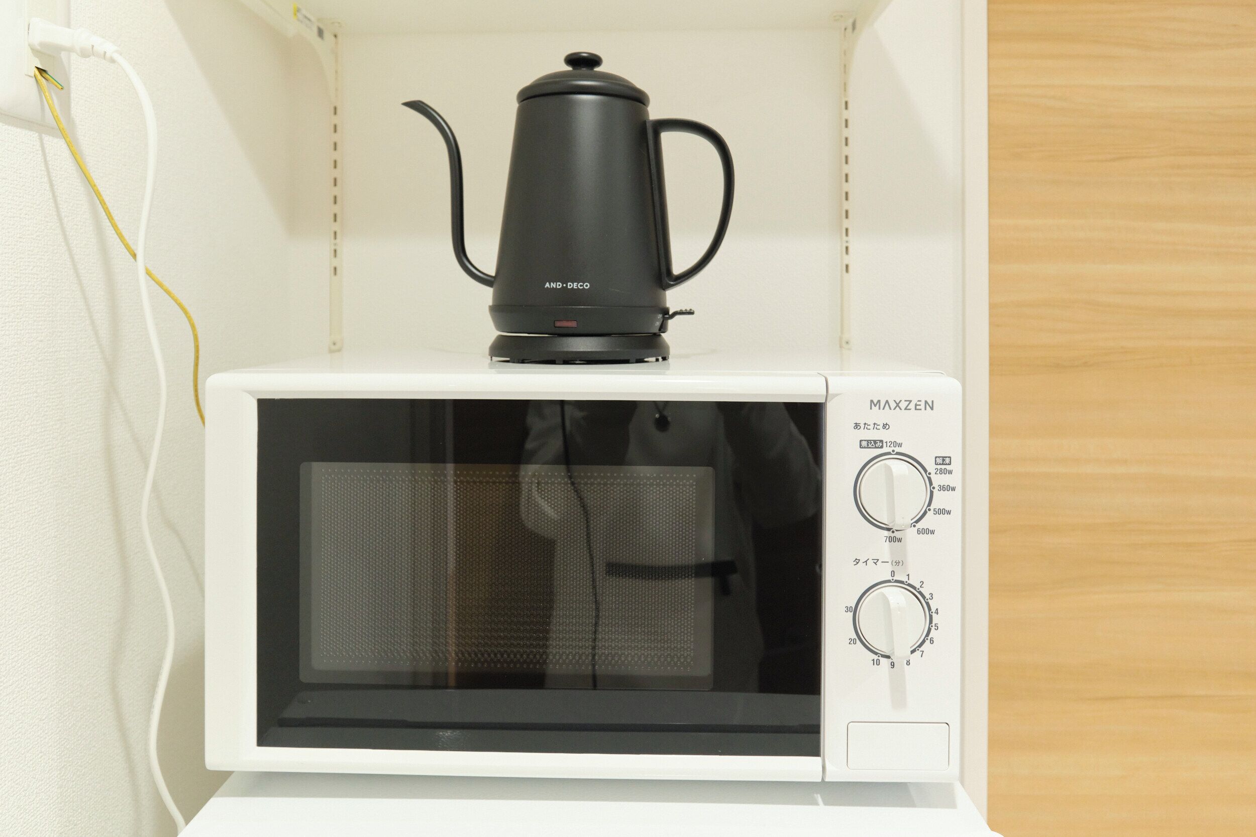 A white microwave with a black coffee pot on top, a power cord, and control knobs.