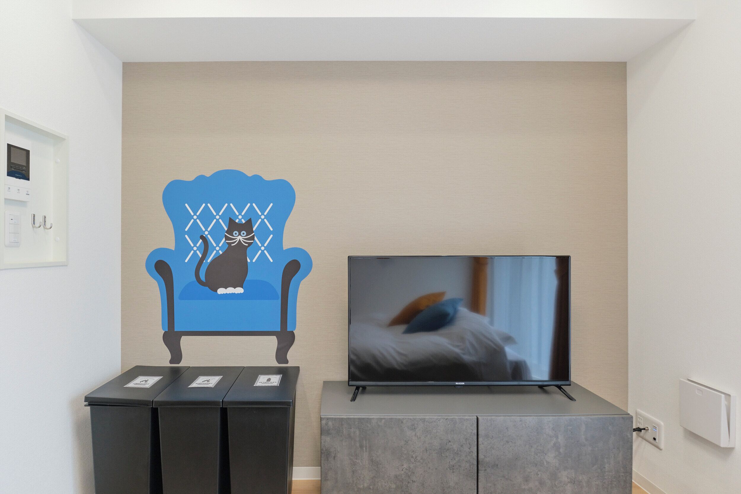 A room with a TV on a stand, a cabinet, and a wall decoration of a cat on a chair.