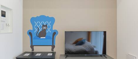 A room with a TV on a stand, a cabinet, and a wall decoration of a cat on a chair.