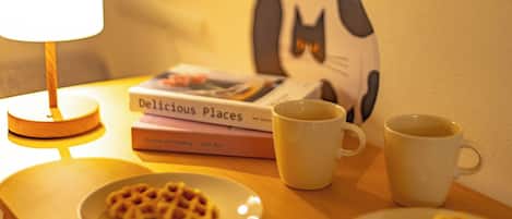 A table with waffles, two mugs, a lamp, and books.