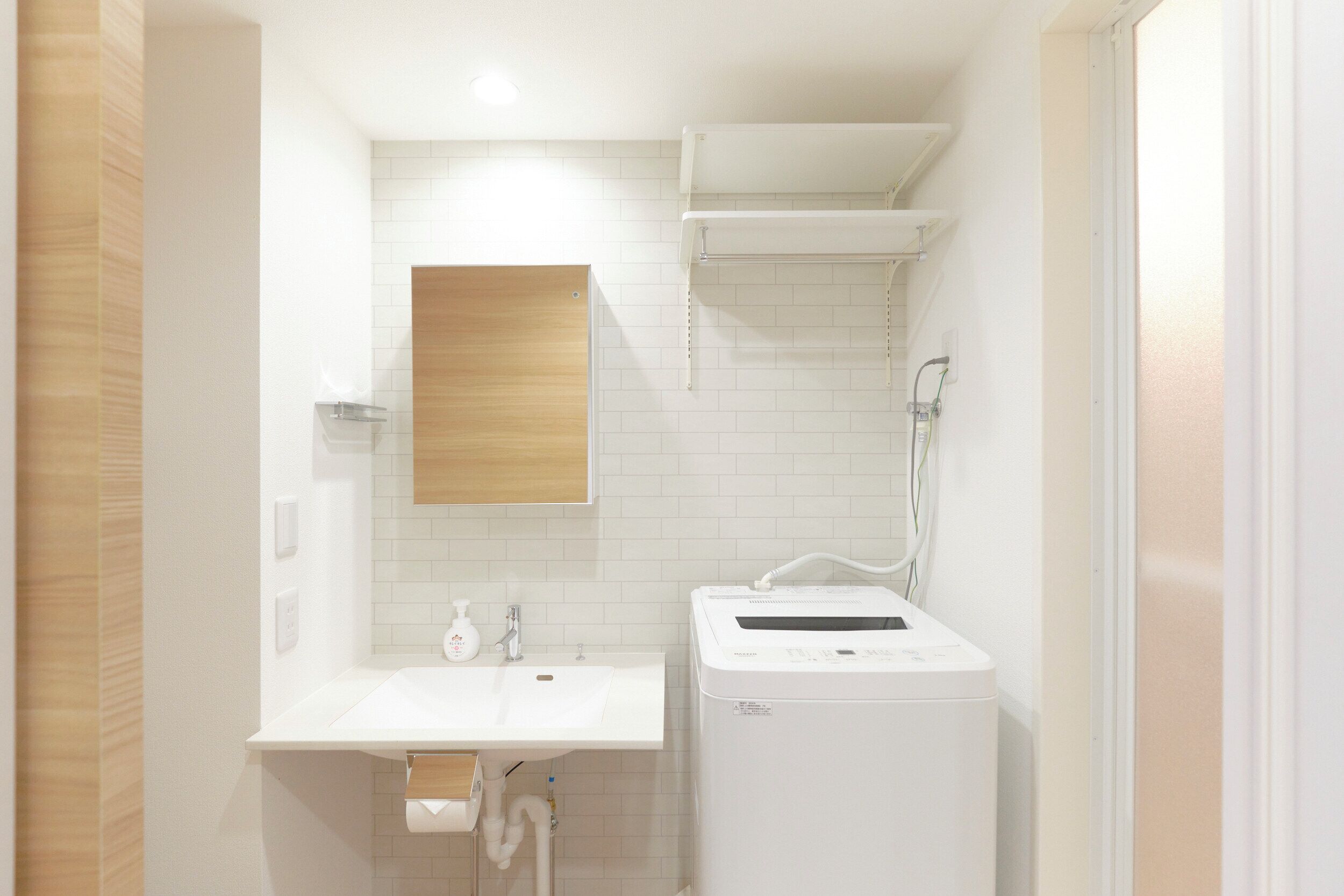 Une salle de bain avec un lavabo blanc, un miroir et un lave-linge blanc.