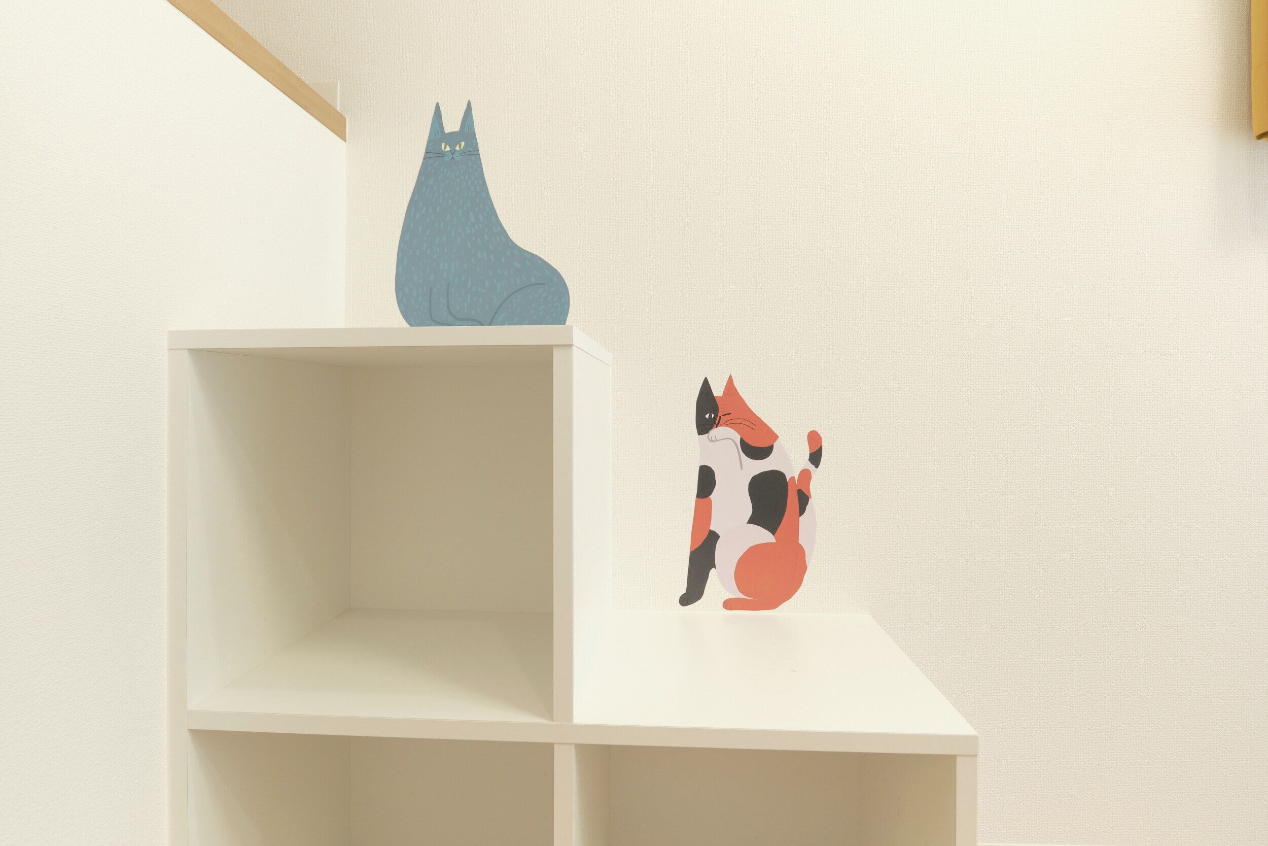 Una estantería blanca con dos ilustraciones de animales; una es un gato azul y la otra, un gato negro y naranja.