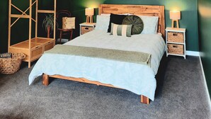 A bedroom with a wooden bed, two bedside tables with lamps, a wooden chair, a green wall, and a small plant. - Whakatā Place - Peaceful, Chic, Central Retreat Near Beaches, Parks & Adventure! (Motueka)