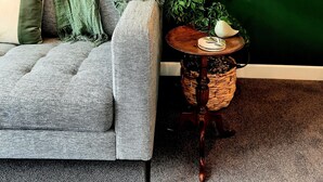 A living room with a grey sofa, a green plant, and a small round wooden side table with a decorative item. - Whakatā Place - Peaceful, Chic, Central Retreat Near Beaches, Parks & Adventure! (Motueka)