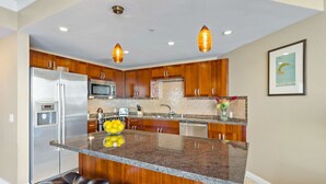 A modern kitchen with wooden cabinets, stainless steel appliances, a granite island, and pendant lighting.
