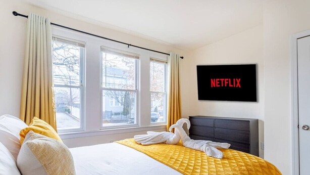 Een hotelkamer met een bed, een aan de muur bevestigde televisie en een raam met gordijnen.