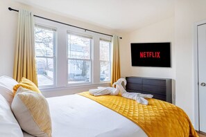 Ein Hotelzimmer mit einem Bett, einem an der Wand befestigten Fernseher und einem Fenster mit Vorhängen.