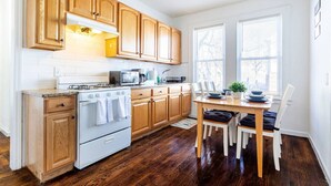 A kitchen with wooden cabinets, a stove, a microwave, and a dining table with chairs. - 2BR Apt| Free Pkng| Netflix|NJ Train| Pets |5 pple (Newark)