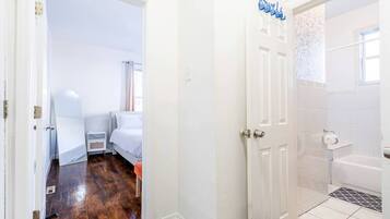 Un dormitorio con una cama, una mesita de noche y una ventana. El baño tiene una bañera, un inodoro y un lavabo.