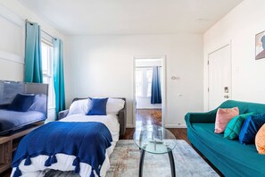 Quarto de hotel moderno com cama, TV, mesinha de centro de vidro e sofá verde-água.