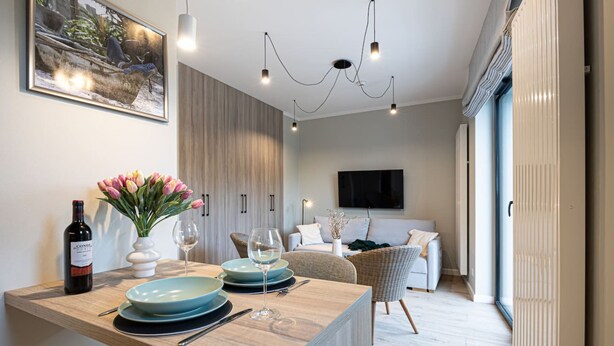 A modern dining area with a wooden table set for two, a wine bottle, and a vase of flowers. - Costa Rogowo Romantyczne Studio Shellter Morze (Trzebiatow)