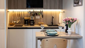 A modern kitchen with wooden cabinets, a dining table with blue plates, and a vase of flowers. - Costa Rogowo Romantyczne Studio Shellter Morze (Trzebiatow)
