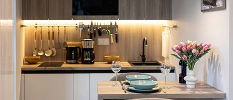 A modern kitchen with wooden cabinets, a dining table with blue plates, and a vase of flowers.