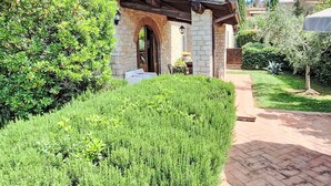 Uma casa de pedra com telhado em telhas, alpendre coberto e um jardim bem cuidado.
