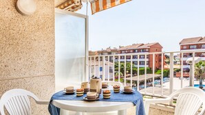 Un balcon avec une table dressée pour le petit-déjeuner, des chaises blanches et une vue sur une piscine et des immeubles.