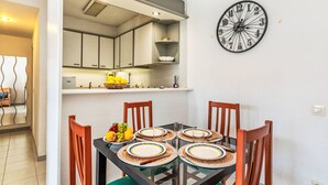 Un coin repas avec une table en verre dressée pour quatre personnes, entourée de chaises en bois. Un panier de fruits et une bouteille sont posés sur la table.