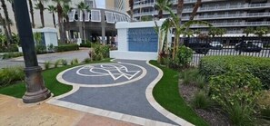 A hotel entrance with a circular logo, palm trees, and a parking area.