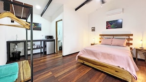 Une chambre avec un lit en bois, un ventilateur de plafond, un bureau avec un lavabo et un petit réfrigérateur.