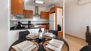 A dining area with a table set for four, a wine bottle, and a kitchen in the background. - Baya de Nerja - Oasis Properties (Nerja)