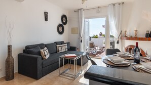 A modern living room with a sofa, a coffee table, and a dining area with a table set for two. - Baya de Nerja - Oasis Properties (Nerja)
