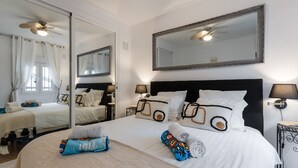 A hotel room with a large bed, a ceiling fan, a mirror, and a bedside table with a lamp. - Baya de Nerja - Oasis Properties (Nerja)