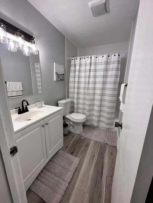 A bathroom with a white sink, toilet, and shower curtain. There is a mirror above the sink and a towel rack on the wall.