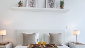 En pænt redt seng med to puder, et sengebord med en lampe, samt et bakke med croissanter og juiceglas.
