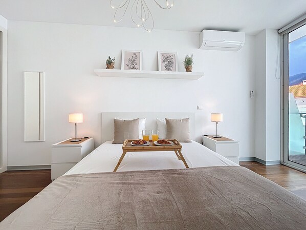 A modern hotel room with a large bed, bedside tables with lamps, a tray with breakfast, and a view of the city through the window. - Acanto Loft by Atlantic Holiday (Funchal)