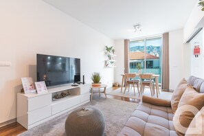 A modern living room with a flat-screen TV, a dining area with a table and chairs, and a large window offering a view of a cityscape. - Acanto Loft by Atlantic Holiday (Funchal)