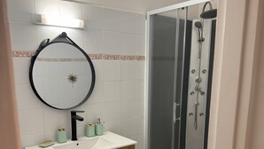 Une salle de bain avec un lavabo blanc, un meuble en bois et une cabine de douche en verre.