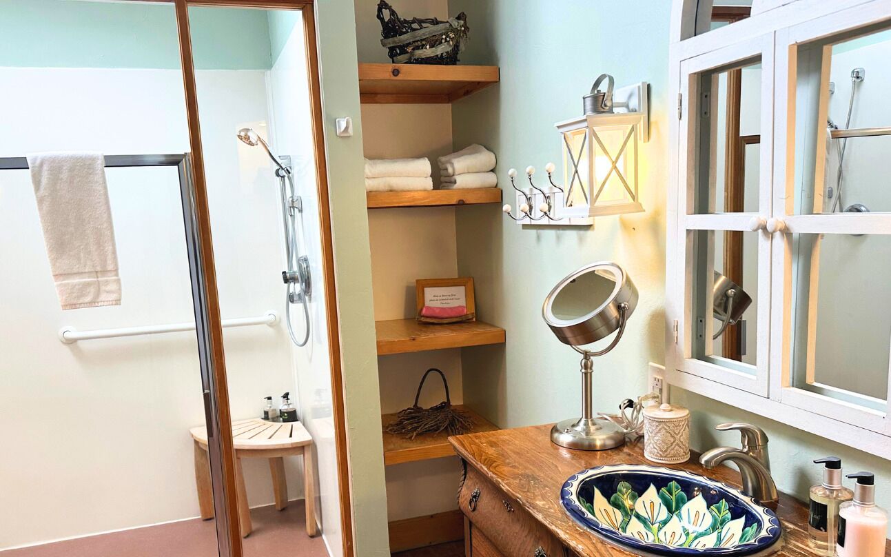 A bathroom with a wooden vanity, a sink with a decorative plate, a towel rack, and a shower area.