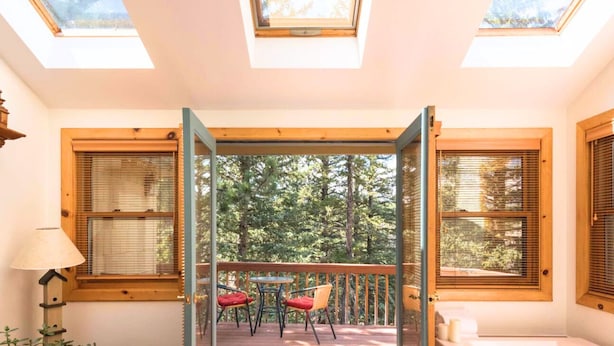 A room with skylights, a balcony with chairs, and a view of trees. - Wood Nymph Suite at RiverSong Inn in Estes Park - Riverside in Rocky Mountain National Park (Estes Park)