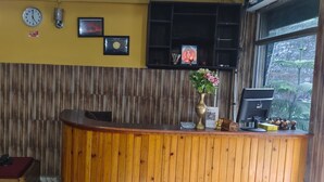 A reception area with a wooden counter, clocks, and a window with a view of greenery. - Hotel parichit (Namchi)