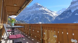 A wooden balcony with a table and chairs, overlooking snow-covered mountains. - Chalet Adlerhorst OG by Interhome (Grindelwald)