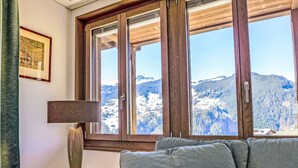 A cozy room with a large window offering a mountain view, a lamp on a side table, and a framed picture on the wall. - Chalet Adlerhorst OG by Interhome (Grindelwald)