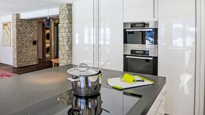 A modern kitchen with a stone accent wall, stainless steel appliances, and a central island. - Chalet Adlerhorst OG by Interhome (Grindelwald)