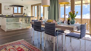 A modern kitchen with a glass island, dining area with chairs, and large windows with a mountain view. - Chalet Adlerhorst OG by Interhome (Grindelwald)
