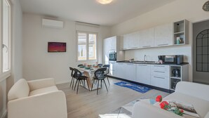 Una cocina moderna con armarios blancos, un comedor con mesa y sillas, y una sala de estar con sofá.