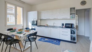 Una cocina moderna con armarios blancos, un microondas y una cafetera. Hay una mesa de comedor con sillas y una alfombra azul.
