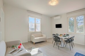 A modern living room with a sofa, dining table, chairs, and a flat-screen TV mounted on the wall. - La Maison Fleurie Appartamento Glicine 2BR Walk Beach, Desenzano Del Garda, Italy (Desenzano Del Garda)