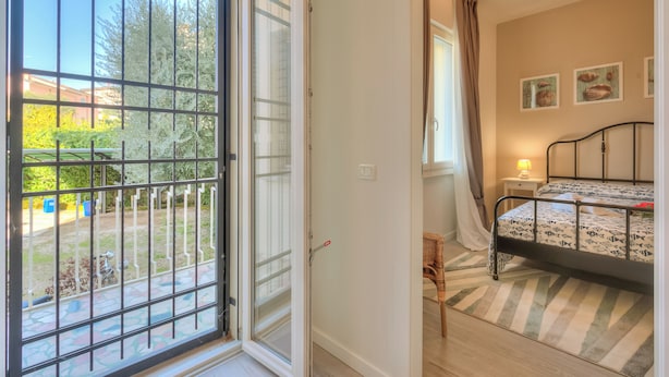 Un dormitorio con cama, mesita de noche, ventana con cortinas y vistas al exterior.
