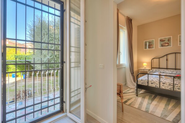 Ein Schlafzimmer mit Bett, Nachttisch, Fenster mit Vorhängen und Blick ins Freie.
