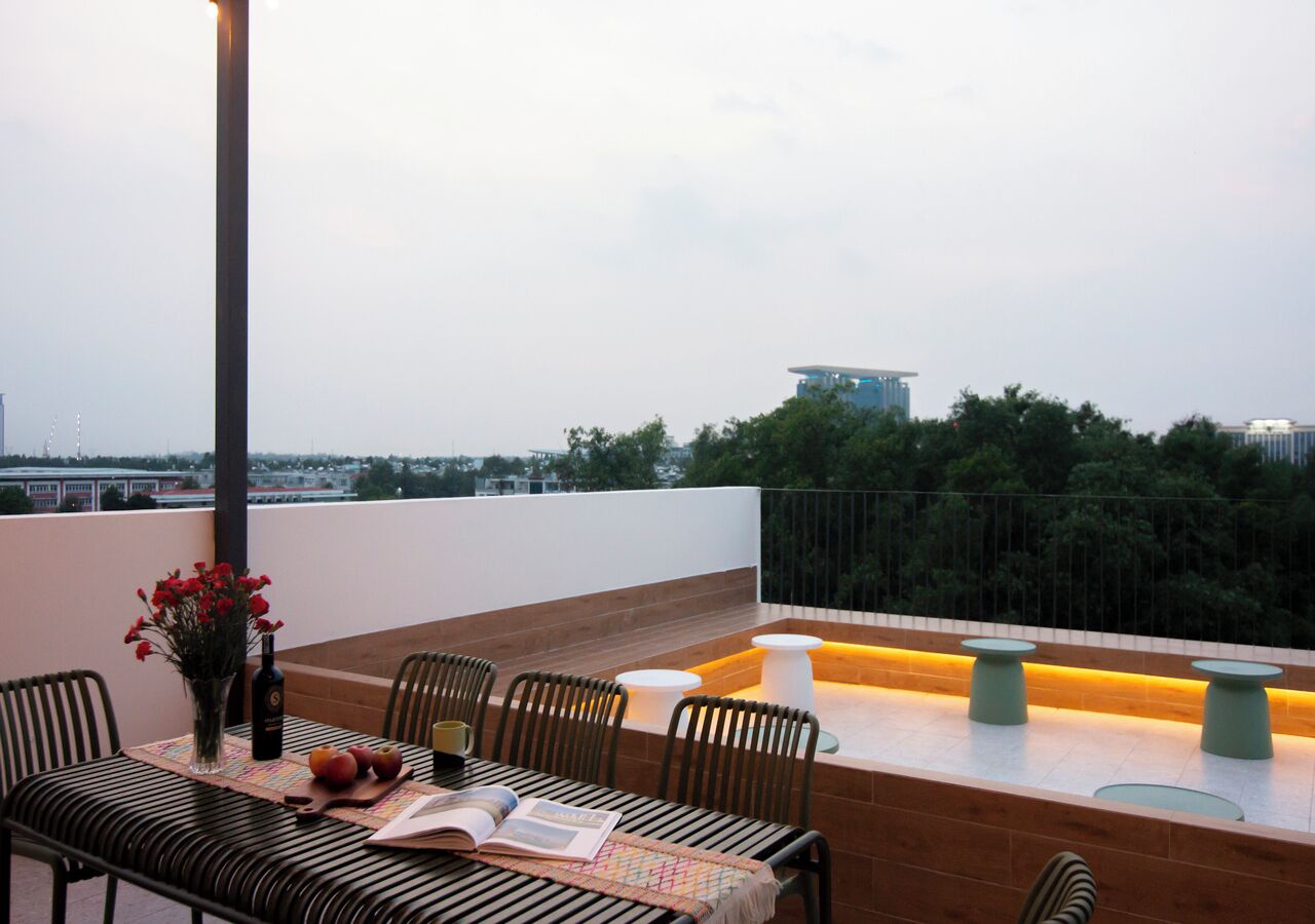 A rooftop terrace with a table set for dining, chairs, a vase with flowers, and a bottle of wine.