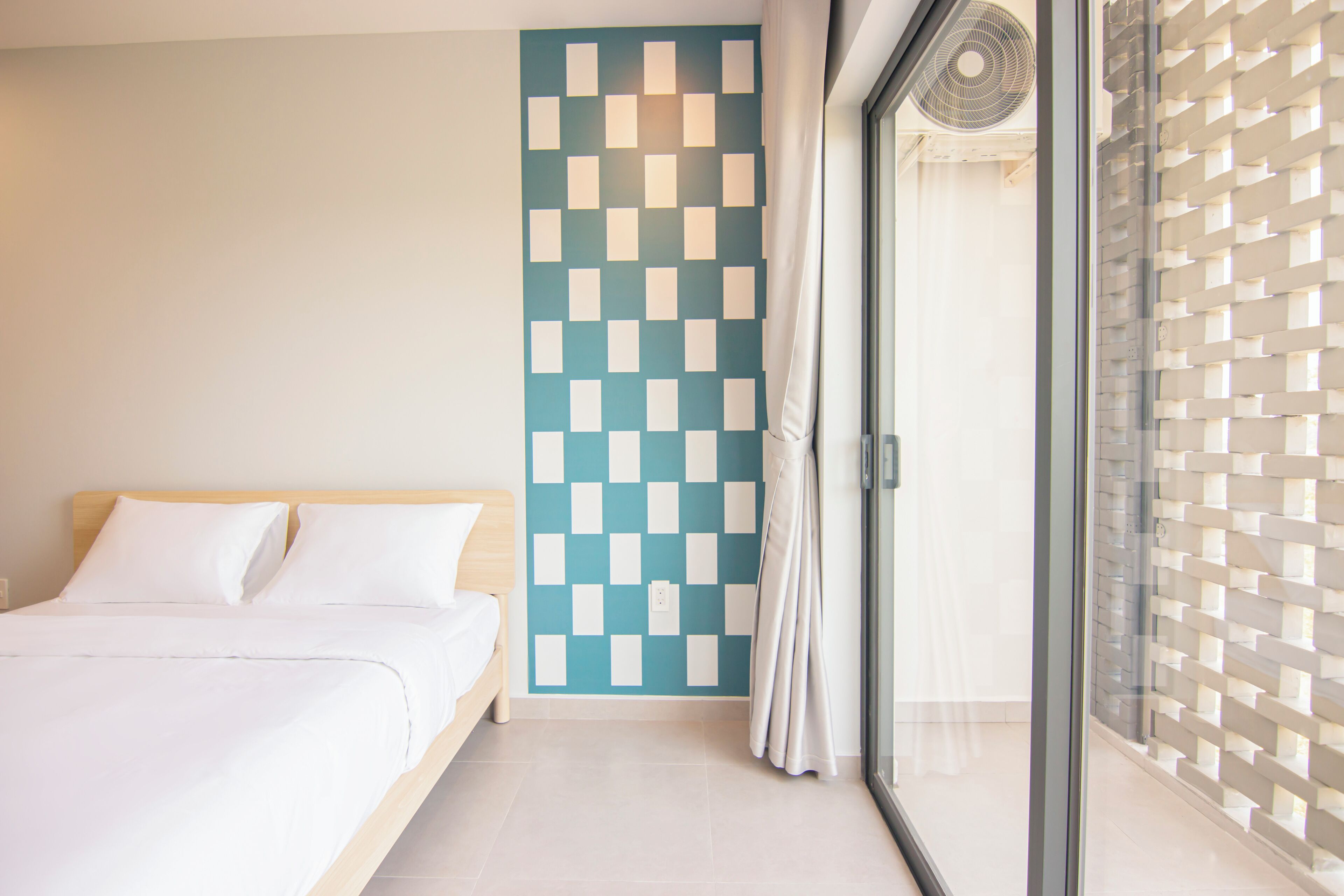 A hotel room with a bed, a checkered wall, a sliding glass door, and a ceiling fan.
